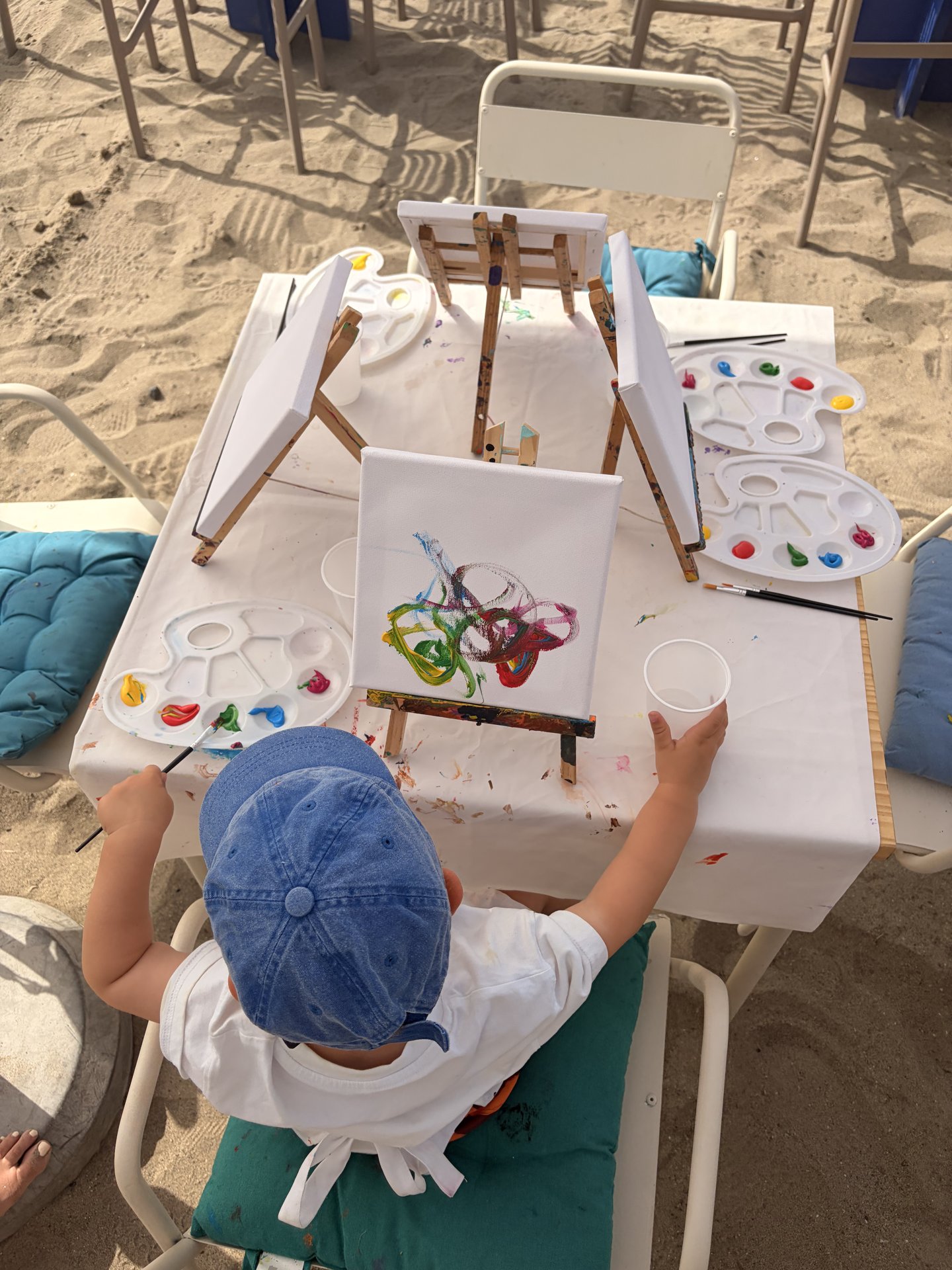 A smiling child holding up a painted canvas covered in colourful splashes
